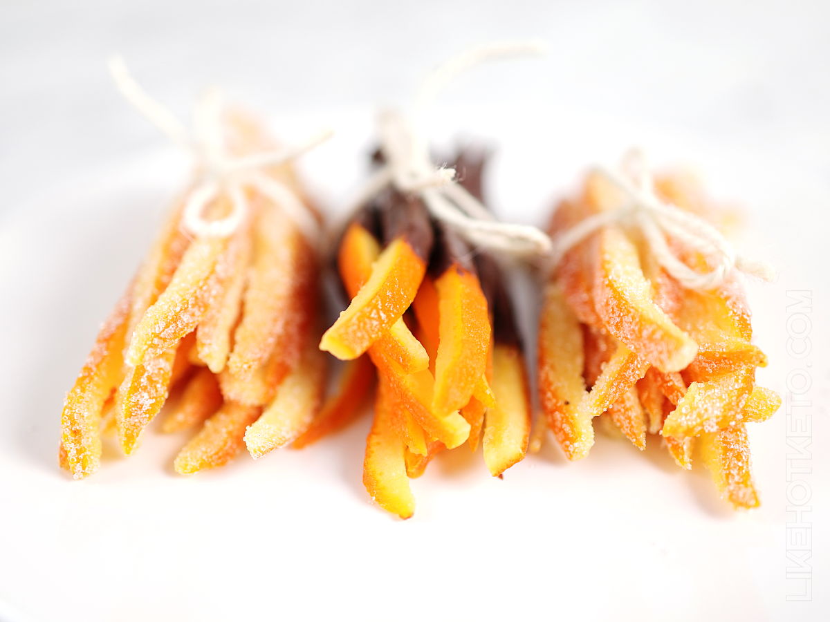 Bundles of keto candied orange peels, dipped in chocolate and in granulated sweetener, tied up with strings on a plate.