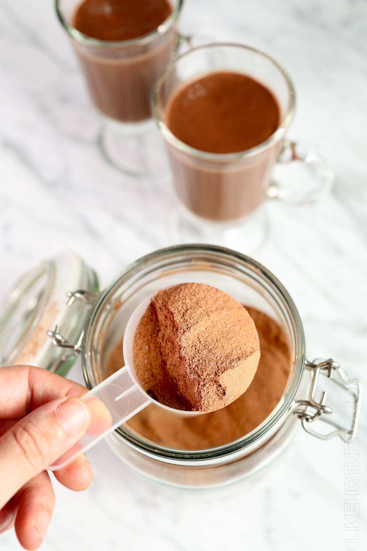 Whey protein keto hot cocoa powder mix being scooped out of jar.