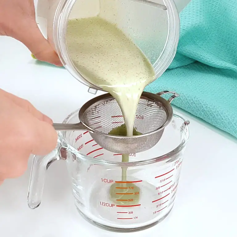 Passing blended milk and mint leaves through a metal strainer.